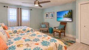 A bedroom with two beds, a ceiling fan, a TV, and a door.