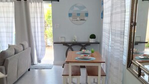 A modern living room with a sofa, a dining table with chairs, a large mirror, and a wall with a circular artwork. - BEACHSIDE COZY GETAWAY! Walk/Bike to Beach,Dining,Bars,Small fenced yard for pet (Naples)