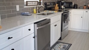 A modern kitchen with white cabinets, a stainless steel dishwasher, a microwave, and a stove. - BEACHSIDE COZY GETAWAY! Walk/Bike to Beach,Dining,Bars,Small fenced yard for pet (Naples)