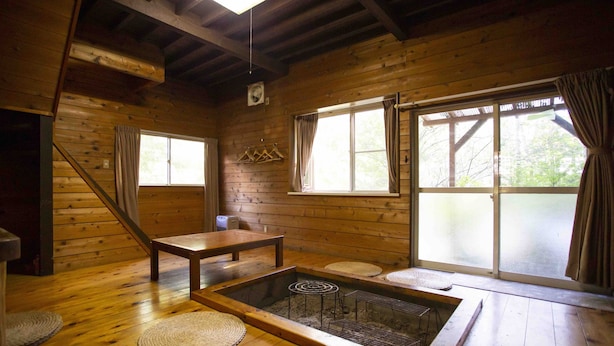 Une cabane en bois avec une table à manger, un petit coin salon et une grande fenêtre avec des rideaux.