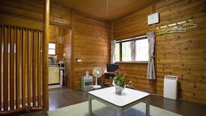 L’intérieur d’une cabane en bois comprend une table à manger, un ventilateur, un téléviseur et un coin cuisine.