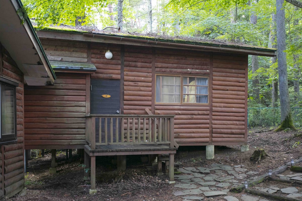 A rustic cabin with a wooden deck, a window with curtains, and a door with a number plate.
