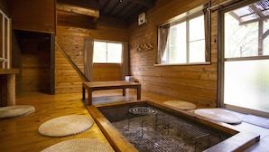 Un intérieur en bois avec une pièce au sol recouvert de tatamis, un bain à eau chaude et une fenêtre avec des rideaux.