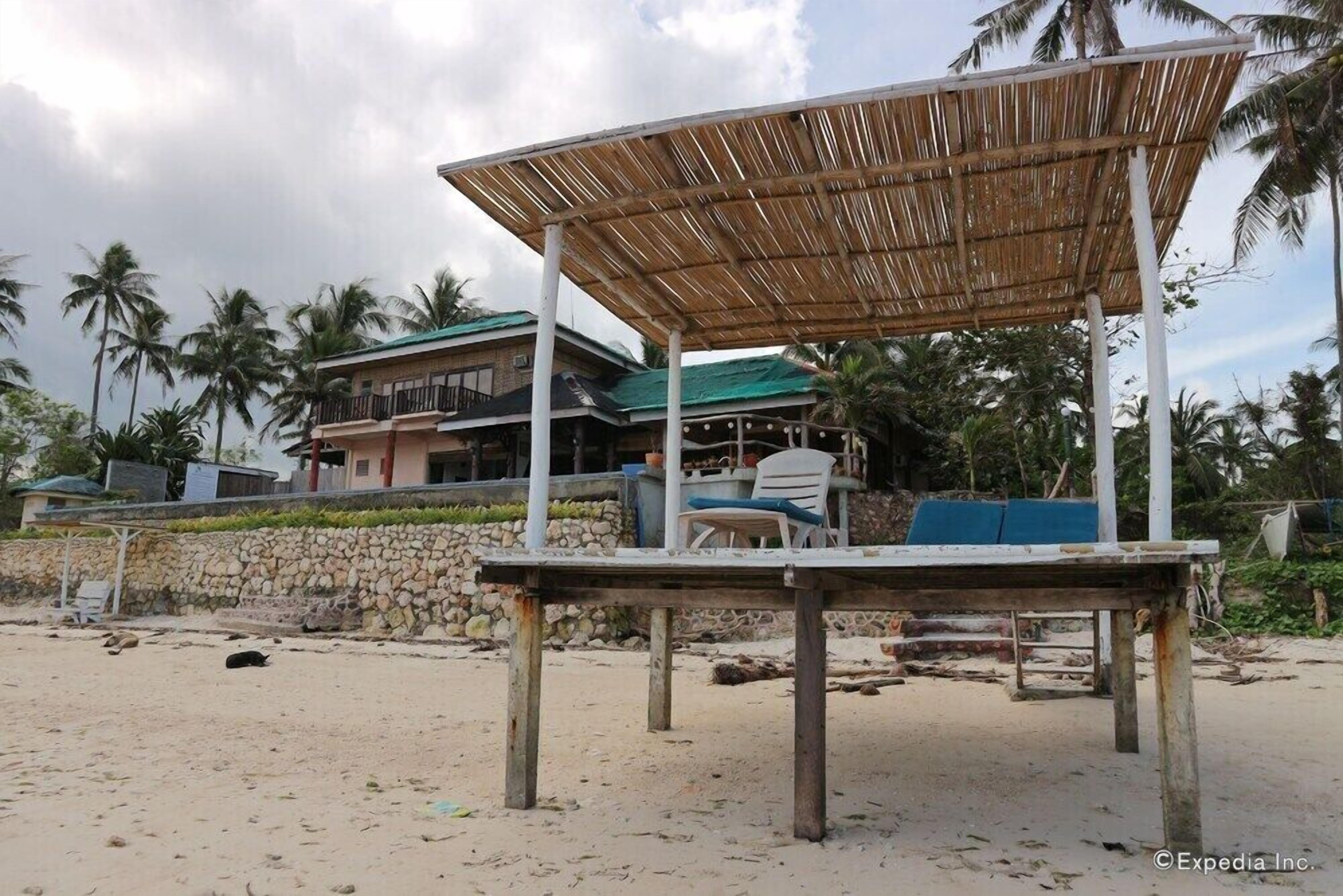 Una estructura frente a la playa con techo de bambú, pared de piedra y una silla blanca.