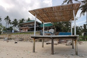 A beachside structure with a bamboo roof, a stone wall, and a white chair. - Blue Wave Inn Beach Resort & Restaurant (Siquijor)