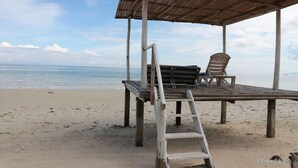 Una cabaña en la playa con terraza de madera, dos sillas y una escalera.