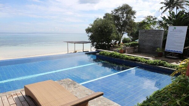 Zona junto a la piscina con vista a la playa, una silla de descanso y un cartel.