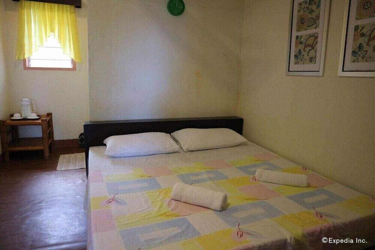 Un dormitorio con una cama, almohadas, una mesita de noche con lámpara y una ventana con cortinas.