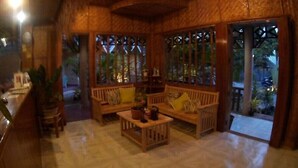 Un rincón de sala acogedor con muebles de madera, una mesita y vista a través de una ventana con celosía decorativa.