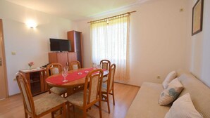 Uma área de jantar com mesa redonda, cadeiras de madeira, toalha de mesa vermelha e uma televisão em um móvel.