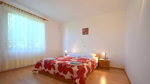 Um quarto com uma cama, duas luminárias de cabeceira, uma janela com cortinas e um pequeno quadro na parede.