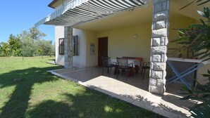 Uma casa com varanda coberta, coluna de pedra e uma mesa com cadeiras.