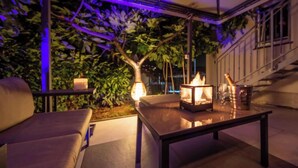 Een terras buiten met een bank, een tafel en een vuurplaats.