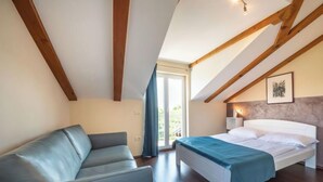 Een slaapkamer met een bed, een bank, houten balken, een raam en een deur.