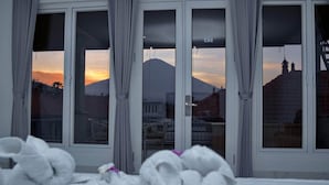 Ein Schlafzimmer mit einem Bett, zwei Fenstern und Blick auf einen Berg sowie Gebäude.