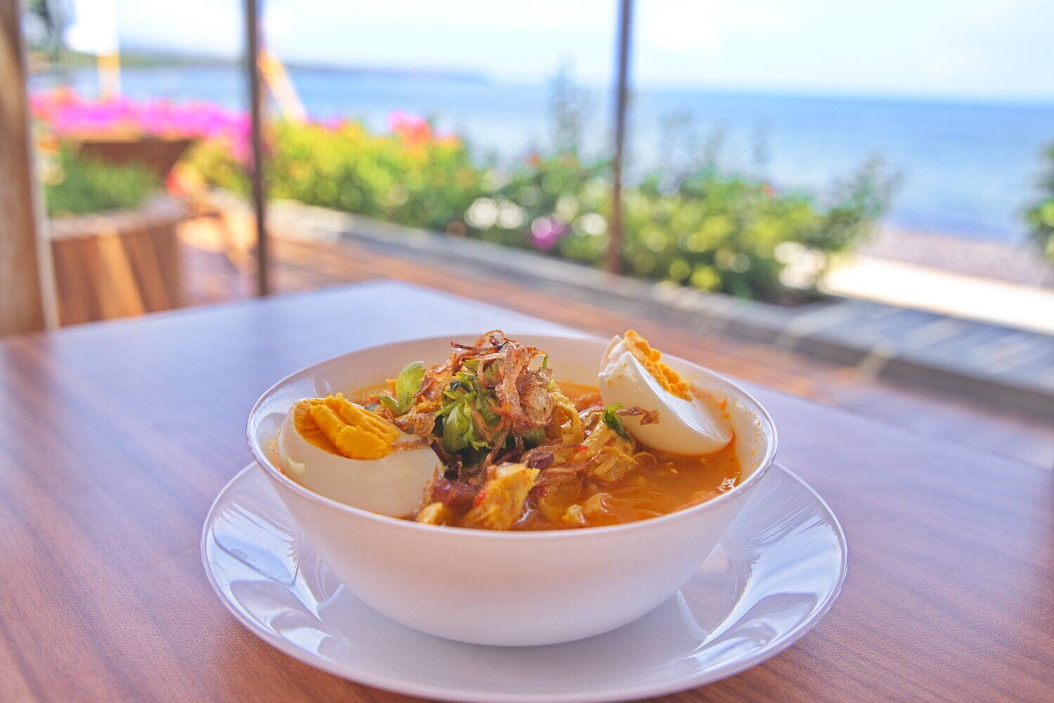 A bowl of food on a table with a view of the sea.