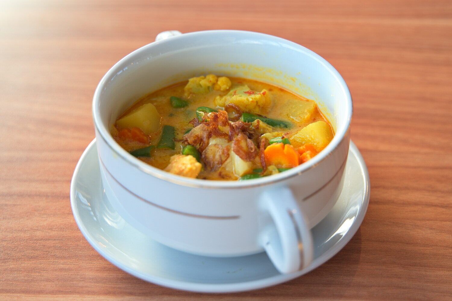 A bowl of soup with vegetables and meat on a wooden table.