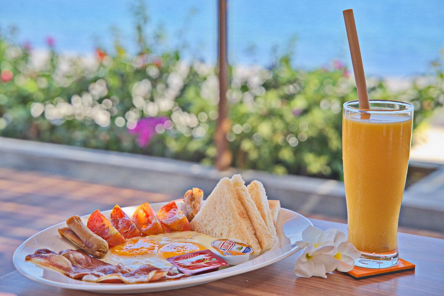 A breakfast plate with toast, eggs, bacon, and a glass of orange juice on a table with a view of greenery and a body of water.