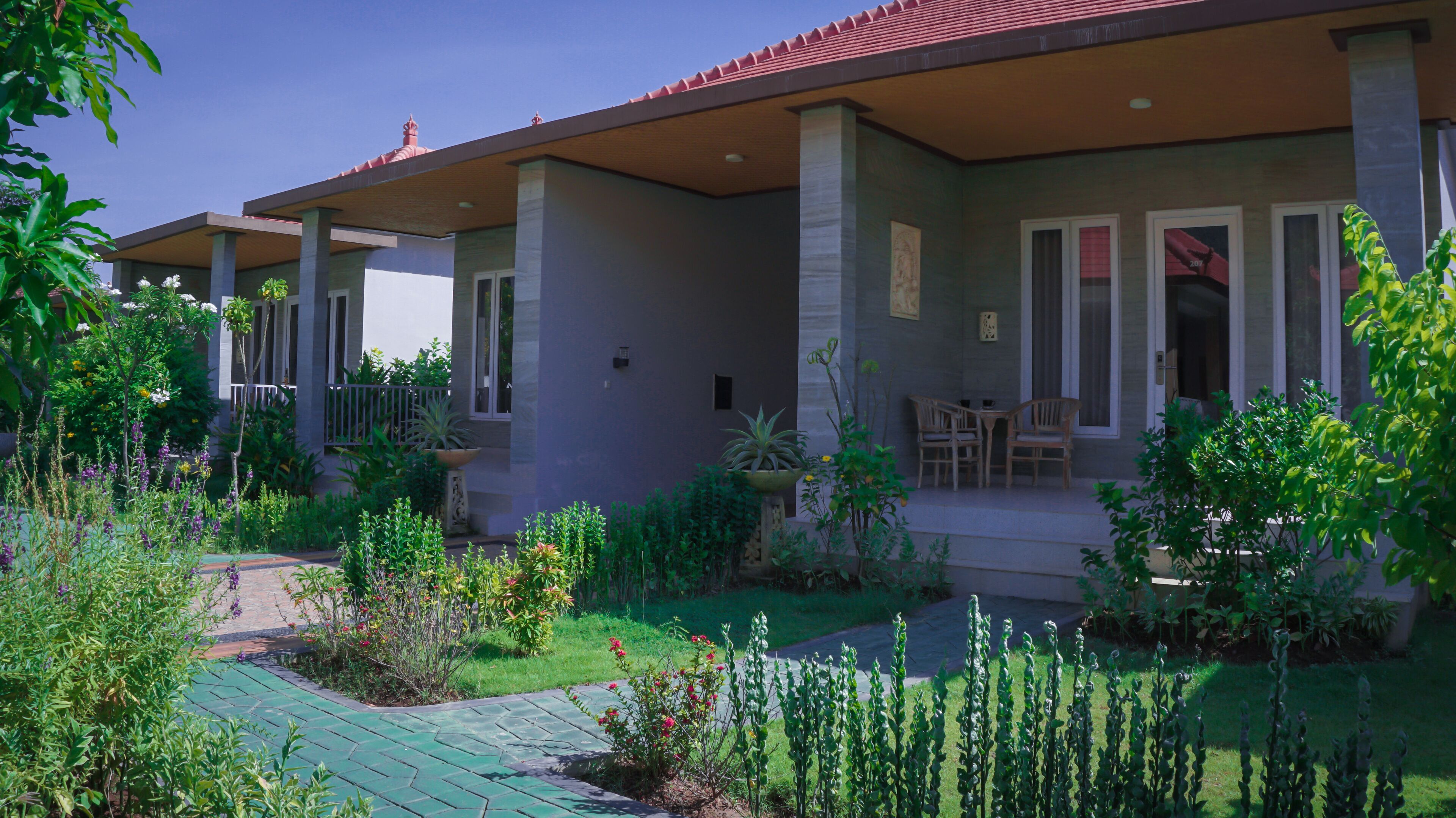 Une maison à deux étages dotée d’un porche abrité, d’un petit jardin et d’une terrasse aménagée avec du mobilier d’extérieur.