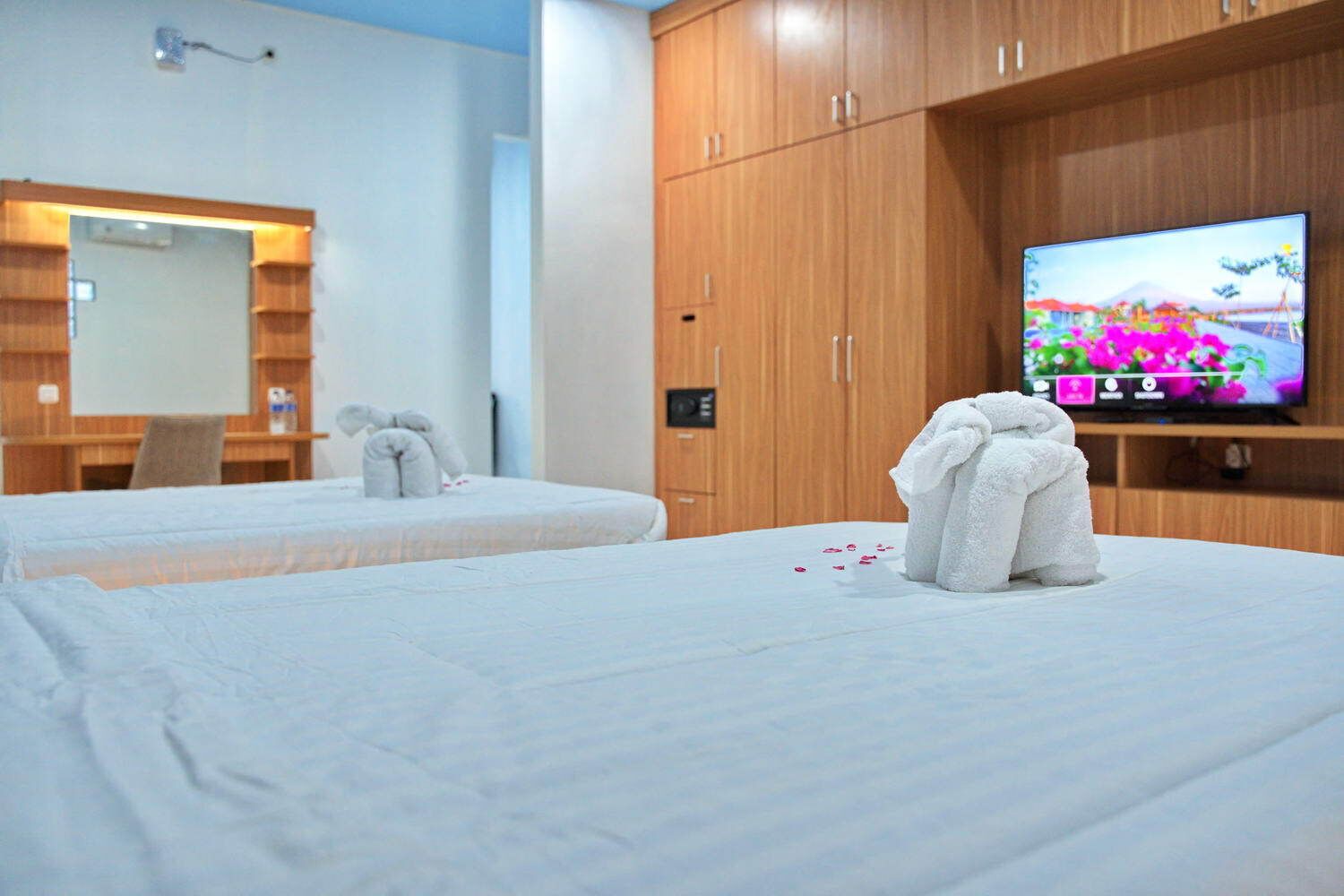 Ein Hotelzimmer mit zwei Betten, einem Fernseher an der Wand, Holzschränken und einem Spiegel.