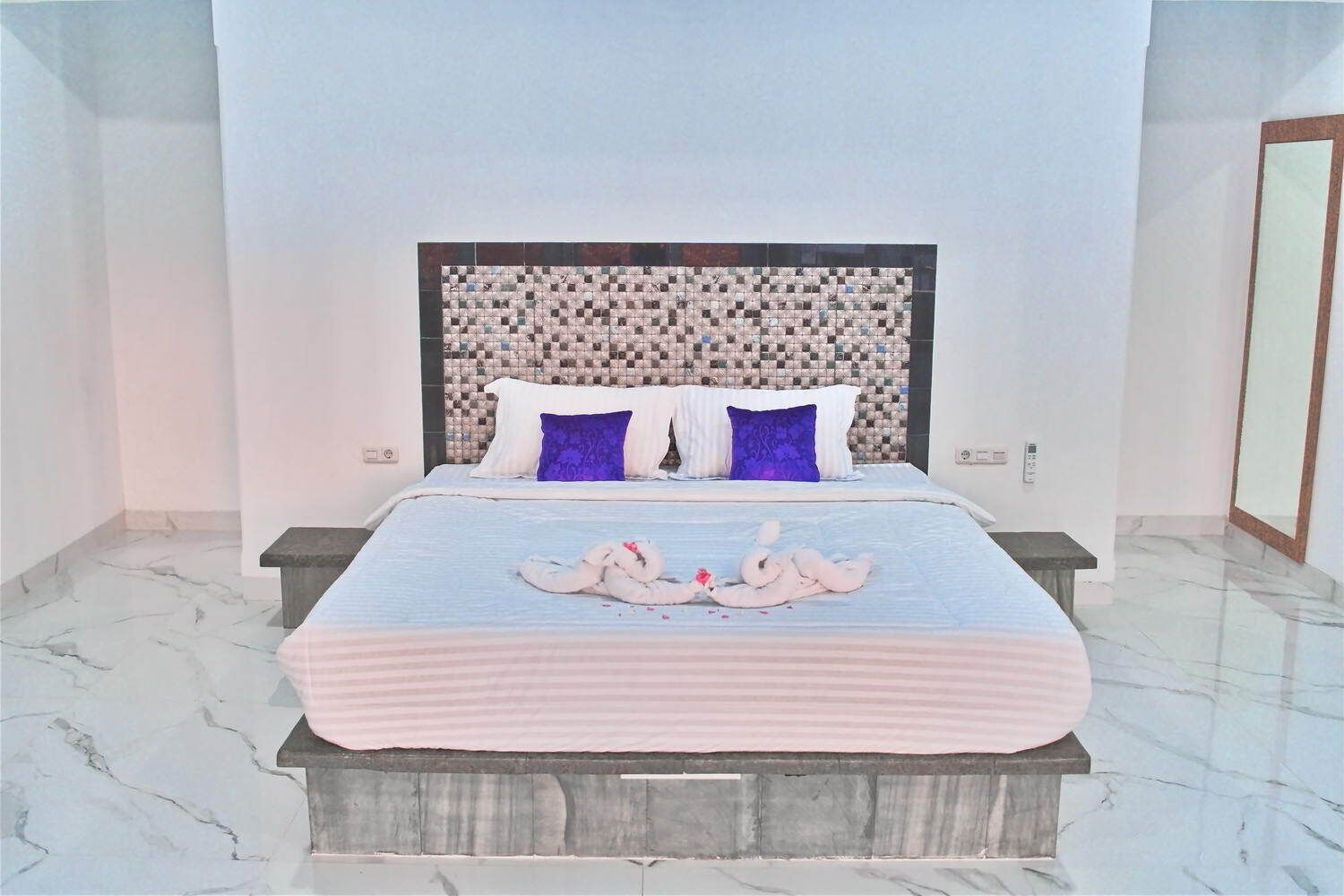 A modern bedroom with a marble floor, a bed with a striped bedspread, two pillows, and a headboard with a mosaic pattern.
