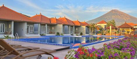 A resort with a swimming pool, lounge chairs, and a mountain backdrop.