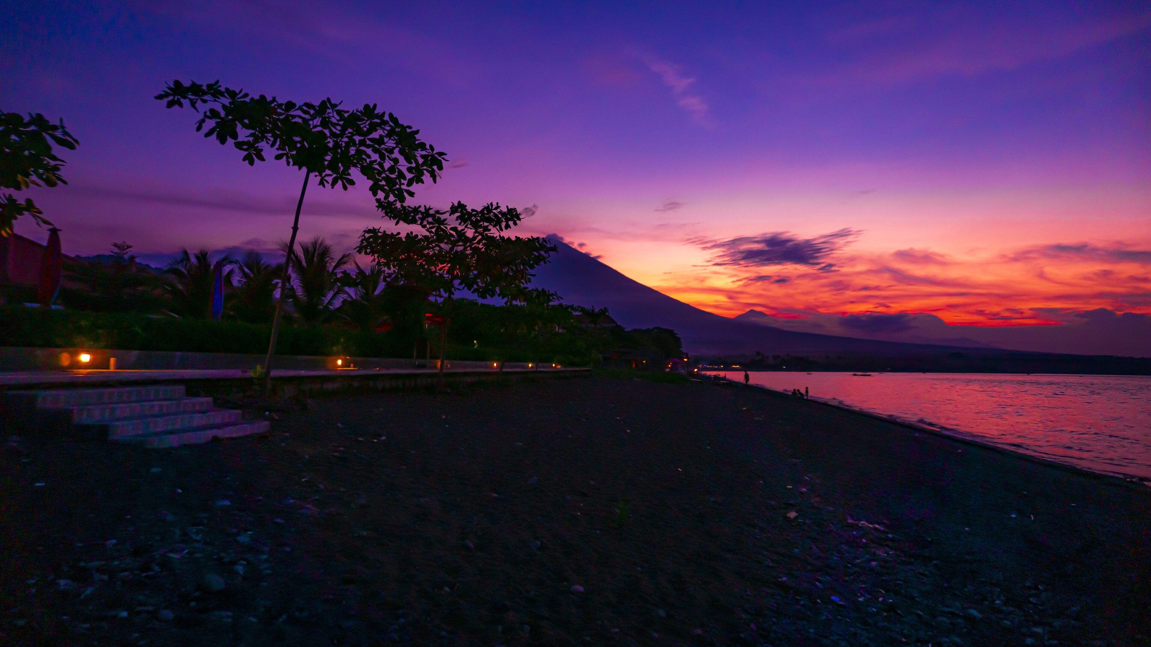 A beach at sunset with a mountain in the background.