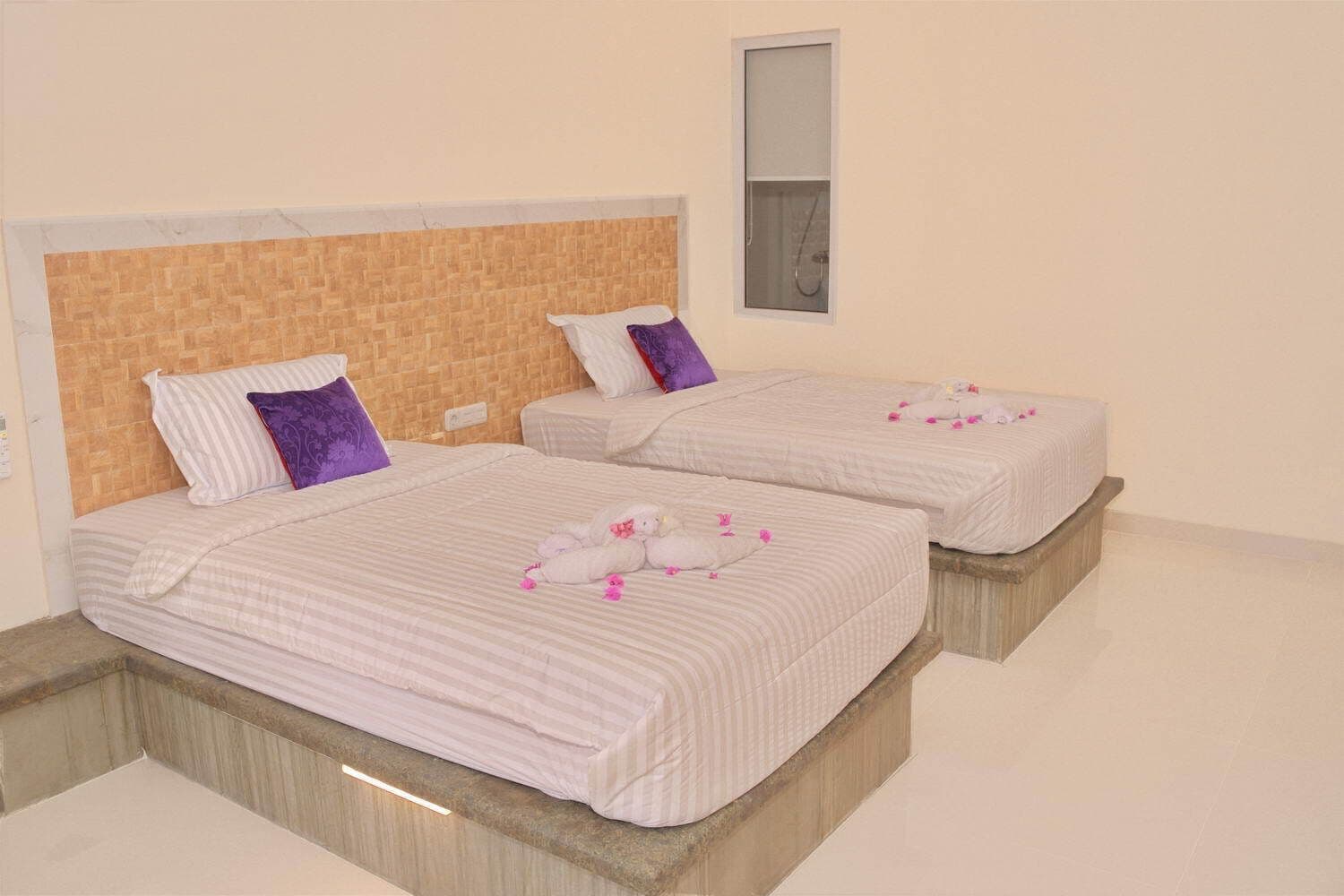 Two single beds with striped bedding, a wooden headboard, and a small window.