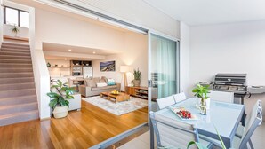 Ein modernes Wohnzimmer mit Glastisch, einer Sofagarnitur, einem Kamin und einer Küchenzeile inklusive Grill.