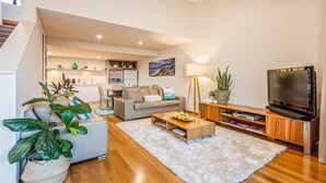 Ein modernes Wohnzimmer mit Sofa, Couchtisch, Fernseher und einer Treppe, die zu einer oberen Ebene führt.