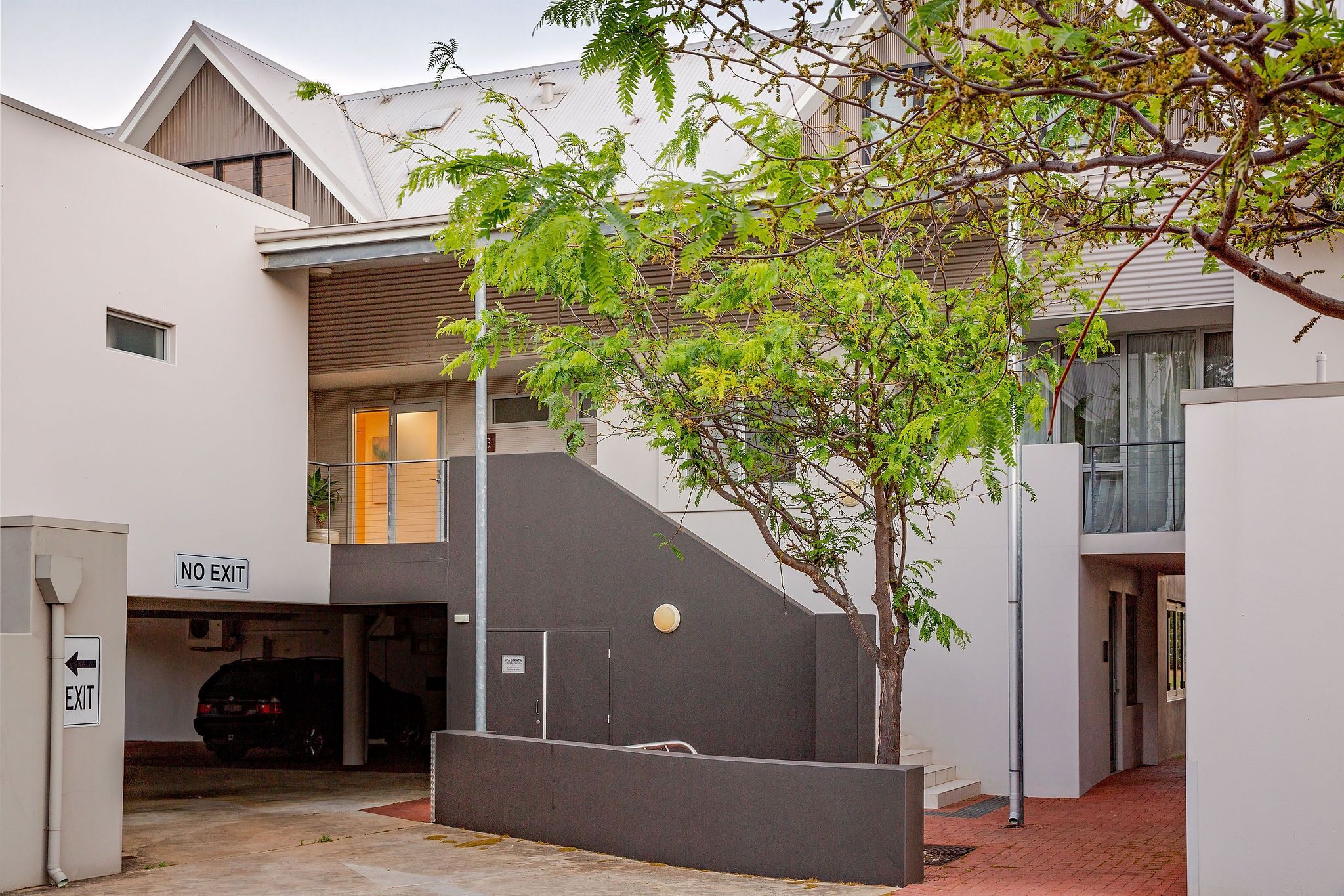 A modern building with a staircase, a car parked in a garage, and a tree in the foreground.