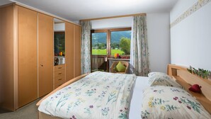 Ein Schlafzimmer mit einem Bett, einem Kleiderschrank, einem Fenster mit Blick auf eine grüne Landschaft und einem kleinen Tisch mit Stuhl.