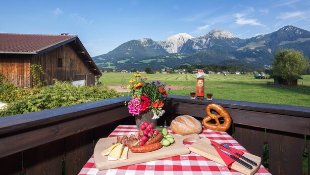 Ein Picknicktisch mit Essen und Blumen, mit Blick auf eine Berglandschaft.