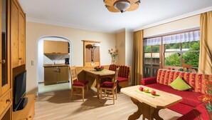 Ein gemütliches Wohnzimmer mit einem roten Sofa, einem Holzespeisesaal und passenden Stühlen. Ein Fernseher ist an einem Holzschrank befestigt, und ein Fenster bietet Blick auf Grünflächen draußen.