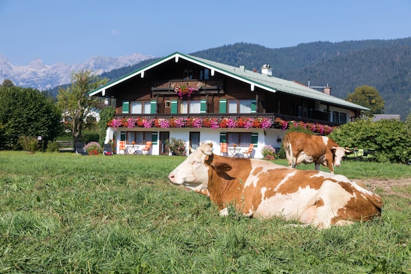 A two-story building with a green roof and a balcony with flowers. - Ferienwohnung Hohes Brett, 2 bis 2 Personen, Appartement, Ostbalkon (Schönau am Königssee)