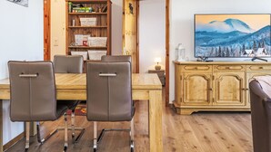 Zona de dinar amb taula de fusta i quatre cadires, armari de fusta amb calaixos i un televisor sobre un prestatge de fusta.