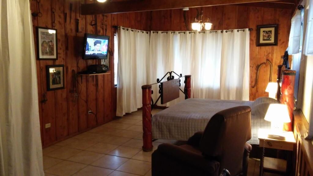 A wooden-paneled room with a bed, a chair, a television, and a lamp.