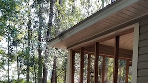 A wooden cabin with a large window, surrounded by trees and a leaf-covered ground. - Lazy Daze! Pups OK, Ideal location! Fenced Yard, Nice House. Wonderful! (Gulf Shores)
