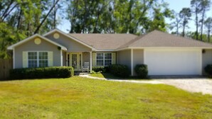 A single-story house with a front porch, a garage, and a well-maintained lawn. - Lazy Daze! Pups OK, Ideal location! Fenced Yard, Nice House. Wonderful! (Gulf Shores)