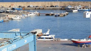 Marina com vários barcos atracados, um molhe de concreto e vista clara do mar.