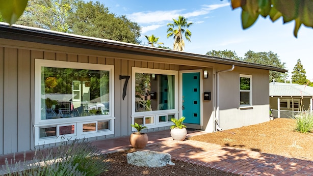 A modern house with large windows, a turquoise door, and a landscaped front yard with plants and a brick pathway.