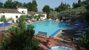 A pool area with lounge chairs and umbrellas, surrounded by greenery and buildings. - Holiday home Two-room apartment for 2 (Pelago)