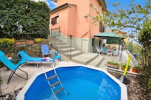 An outdoor swimming pool with a ladder, blue lounge chairs, and a covered patio area. - Casale Geniva with private pool, Massarosa, Italy (Massarosa)