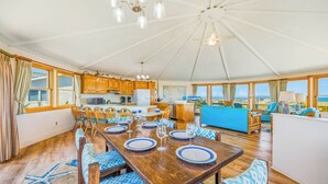 Amplia habitación con comedor, cocina y zona de estar junto a un ventanal con vistas al mar.