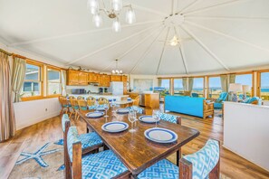 A spacious room with a dining area, kitchen, and seating by a large window overlooking the sea. - Oceanfront Dog Friendly w/ Hot Tub, Game Room, Community Pool/Tennis/Pickleball (Avon)