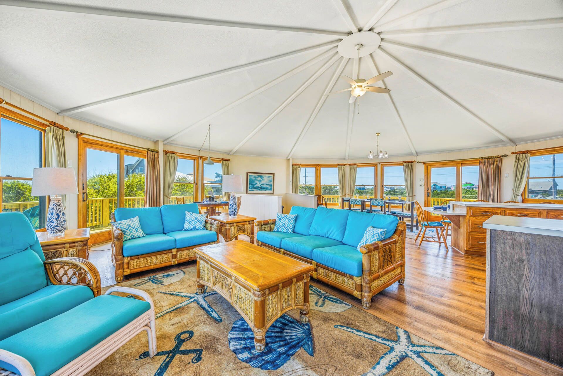 A spacious sunroom with a high ceiling, large windows, and a central seating area with a wooden coffee table.