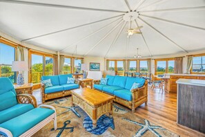A spacious sunroom with a high ceiling, large windows, and a central seating area with a wooden coffee table. - Oceanfront Dog Friendly w/ Hot Tub, Game Room, Community Pool/Tennis/Pickleball (Avon)