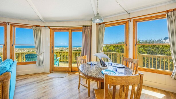 Una habitación con una mesa de comedor, sillas, una lámpara colgante y ventanas amplias que ofrecen vistas a la playa.
