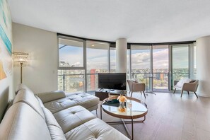 Enjoy expansive city views from the large glass wall in this stylish living room, featuring a plush sofa, coffee table, and armchairs.