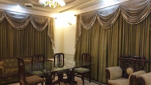 A formal dining room with a glass table surrounded by chairs, a sofa, and a decorative console table. - Chinese Guest House (Lahore)
